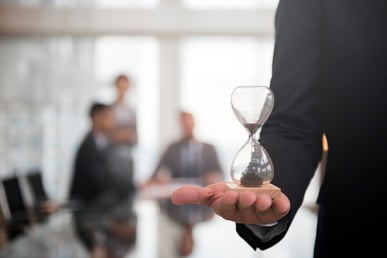 L'image montre un homme en costume tenant un sablier dans sa main, qui symbolise l'importance de la gestion du temps. Cette image représente l'idée de la gestion efficace du temps dans un contexte professionnel.