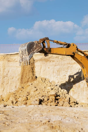 Cette image montre une pelleteuse en action sur un chantier de construction, versant de la terre et des cailloux. L'image illustre le processus d'excavation, élément essentiel dans les travaux de terrassement et la préparation des terrains pour la construction.